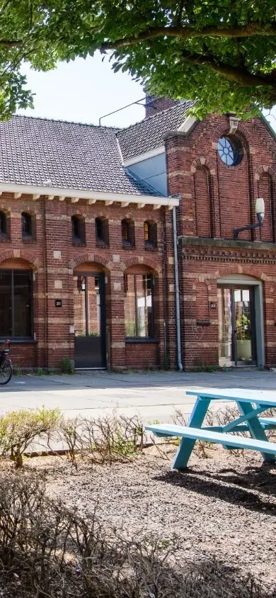 Exterieur van een roodbakstenen gebouw op de Westergasfabriek in Amsterdam, met grote glazen ramen en traditionele architectuur